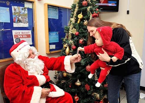 A child in a red suit meeting Santa beside a decorated tree