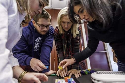 Four people leaning over a table working through a puzzle together