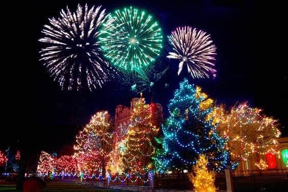 Fireworks bursting above a park lit with Christmas light displays