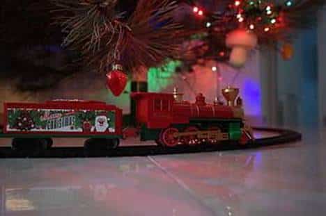 Model steam train running on a track beneath a decorated Christmas tree